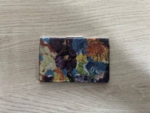 Etui z kolorowym wzorem kwiatowym, zamknięte, leżące na drewnianej powierzchni.